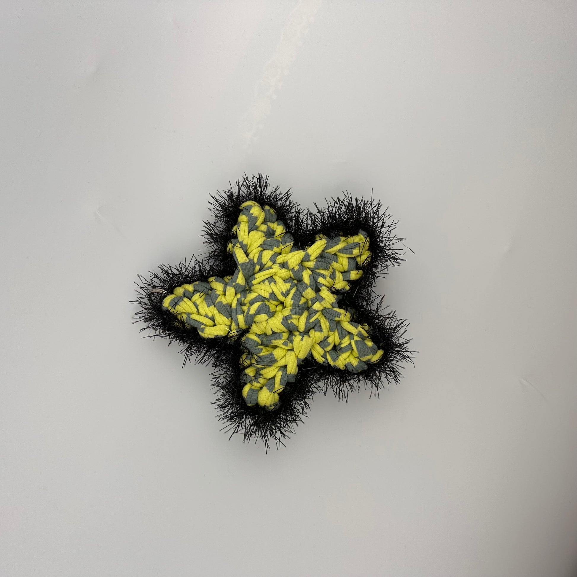 Star-shaped bag charm yellow and grey t-shirt yarn with black tinsel on a light gray background