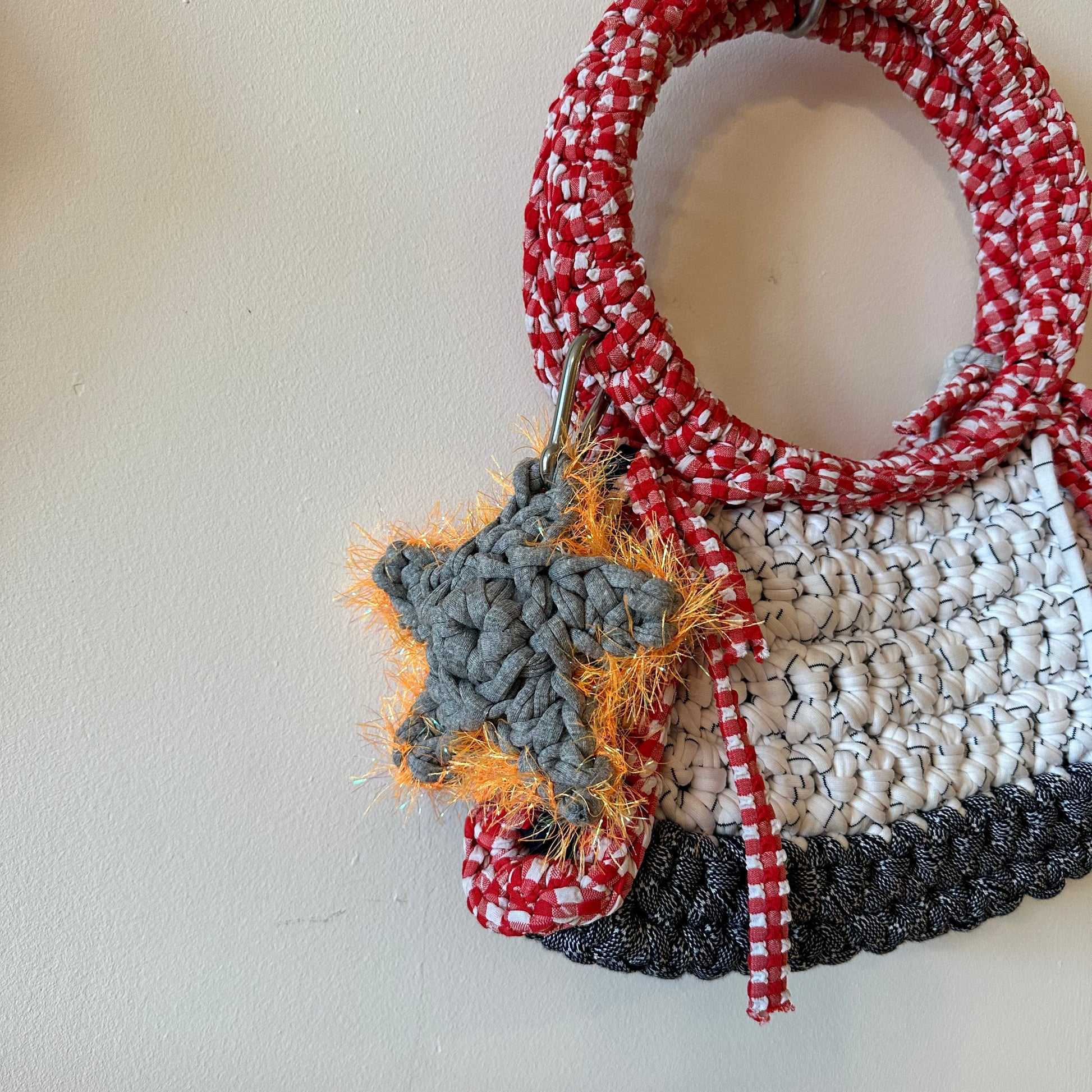 Crocheted star grey & orange Bag charm, with a Sloe Mosey red and white bag, against a white background. 